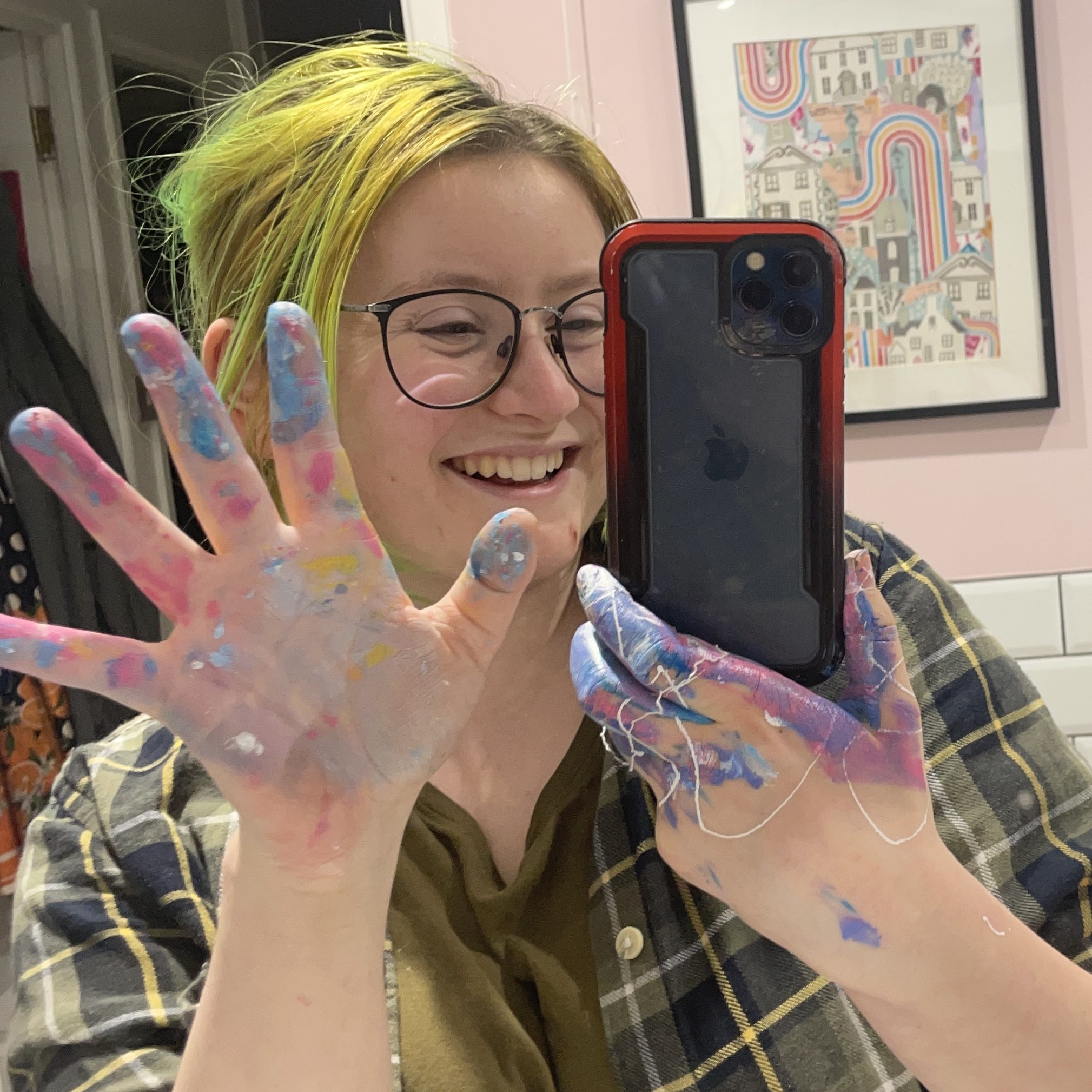 Freddie, a white person with green hair, poses with colorful splatters of paint on his hands.